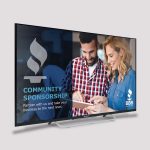 A TV screen displays a community sponsorship ad with two people smiling and looking at a tablet. The BBB logo and tagline are visible on the ad.