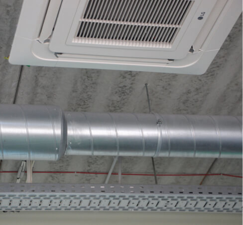An LG ceiling-mounted air conditioning unit installed next to exposed metal ductwork and a cable tray on a concrete ceiling.