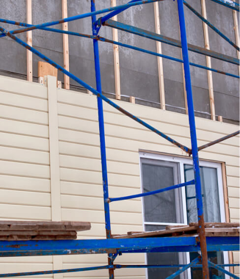 Blue metal scaffolding erected in front of a building with partially installed siding.