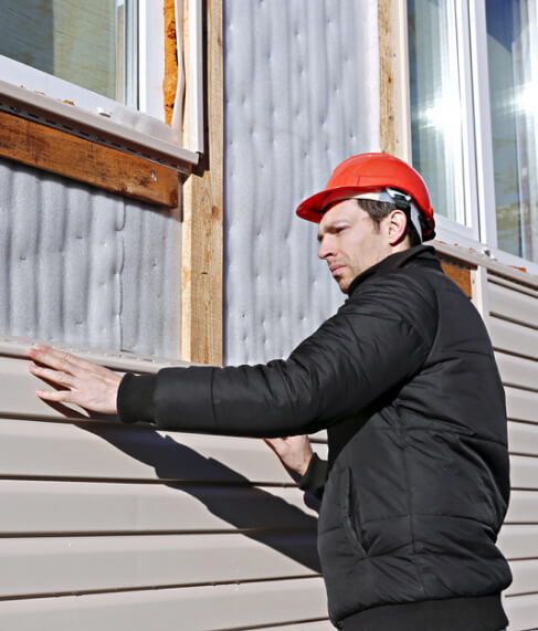 A construction worker in a red hard hat installing siding on the exterior of a building.