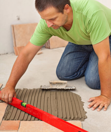 img - man-laying-ceramic-floor-tiles-checking-lines-with-a-level-