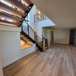 Modern interior with wooden flooring, open staircase with metal railing, white walls, and scattered toys on the floor near a doorway.