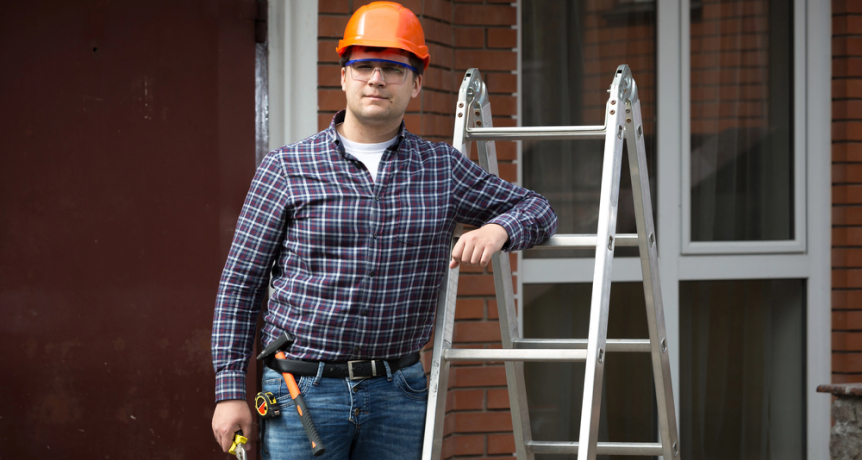 img - smiling-worker-in-hard-hat-leaning-against-metal-ladder