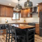 Modern kitchen with wood cabinets, black appliances, a central island with seating for two, pendant lights, and white subway tile backsplash.